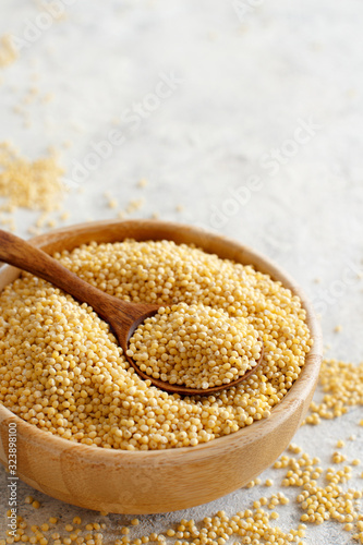 Raw dry hulled millet in a wooden bowl with a spoon