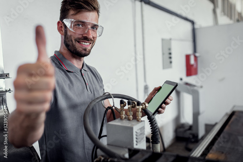 Young engineer setup plasma cutter for work in metalwork workshop, shoeing thumbs up.