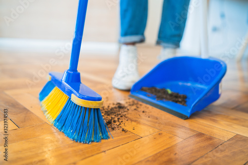 Latin man sweeping wooden floor with broom at home.