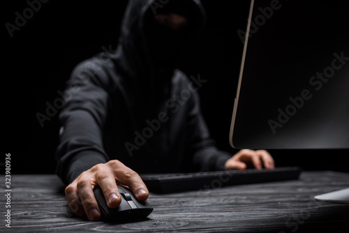 selective focus of computer mouse in hand on hacker isolated on black