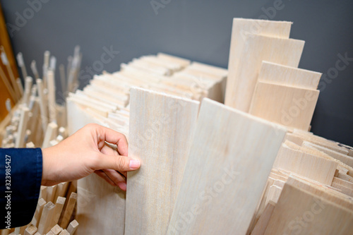 Male hand designer choosing beige balsa wood plank in stationery shop. Wooden material for making art and craft model. Wood industry concept