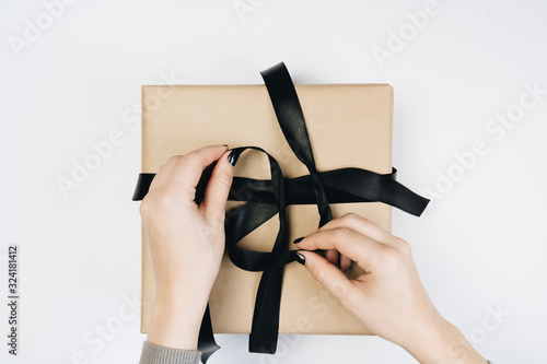 Partial view of woman tying ribbon on gift box isolated on white