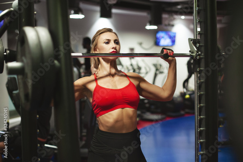 Beautiful young athletic woman is training in the gym. A girl in sportswear performs exercises with a barbell. Workout, sport, fitness, style, lifestyle