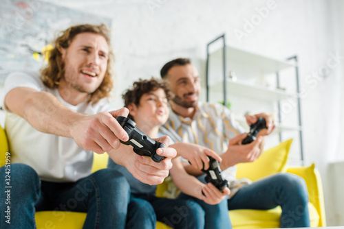 KYIV, UKRAINE - JANUARY 28, 2020: selective focus of cheerful homosexual couple playing video game with mixed race son