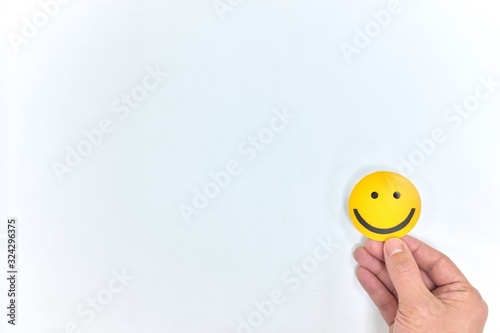 A hand holding a yellow happy face in white background with copy space. Positive customer feedback and review. Happiness and Good service concept.