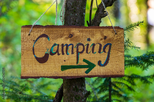 A soft focus closeup view of a handcrafted wood directional campsite sign, woodland camping during multicultural festival celebrating earth and nature
