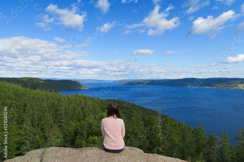 Beautiful young woman sitting while contemplating the Saguenay fjord in peace