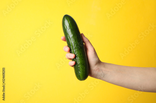 Female hand holding cucumber on yellow background, space for text