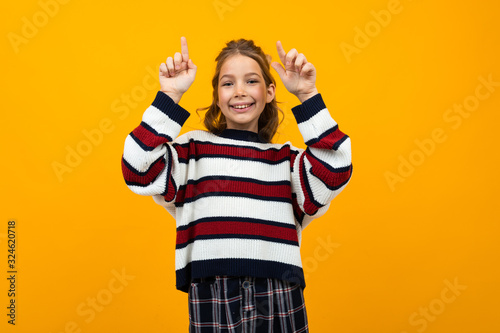 cute teen girl in a striped casual sweater shows on the wall with copy space