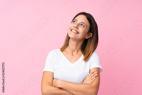 Young woman over isolated pink background looking up while smiling