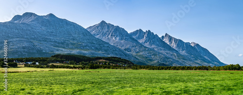 Panoramic view at five of Seven Sisters Mountain range on Sandnessjoen, ideally green grass, small Norwegian village and mountains beside the field. Shinny sunny day, blue skies, Norway, copy space