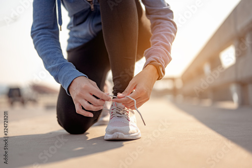 Young women using their hands to tie their shoes jogging in morning workout at the city. A city that lives healthy in the capital. Exercise, fitness, jogging, running, lifestyle, healthy concept..
