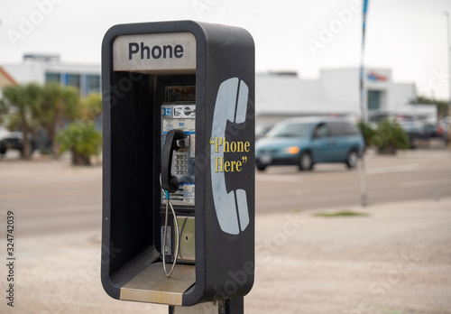 Public Pay Phone, coin operated, next to a busy street is an old and dirty analog type, but still in working condition as traffic drives by in background.