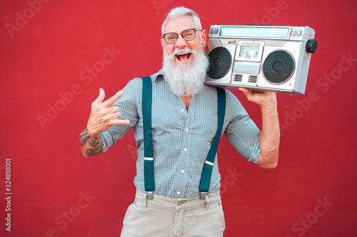 Senior crazy man with 80's boombox stereo playing rock music with red background - Trendy mature guy having fun dancing with vintage radio - Joyful elderly lifestyle concept - Focus on his face
