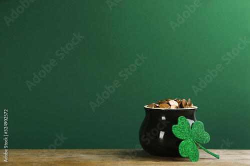 Pot of gold coins and clover on wooden table against green background, space for text. St. Patrick's Day celebration