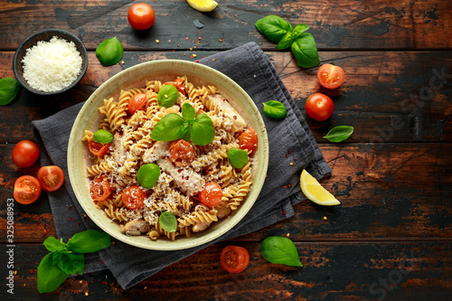 Healthy Chicken, fusilli pasta with tomatoes, basil and parmesan cheese. on wooden table.