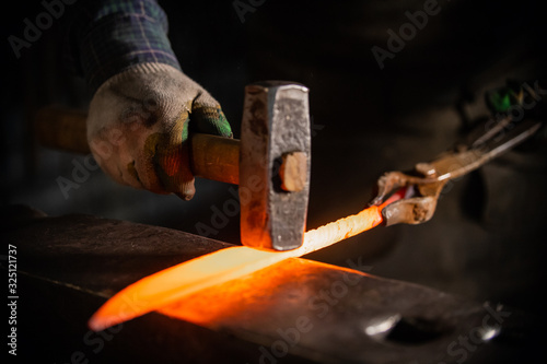 Forging a knife out of the hot metal using a hammer - holding the knife in forceps