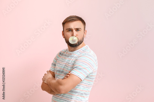 Funny man with chewing gum on color background