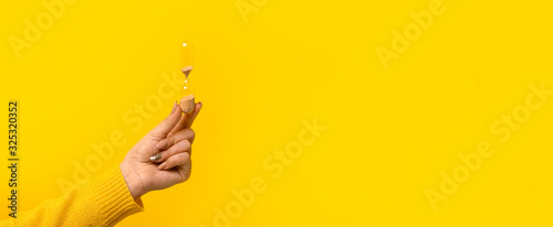 hourglass in hand over yellow background, panoramic mock-up with space for text