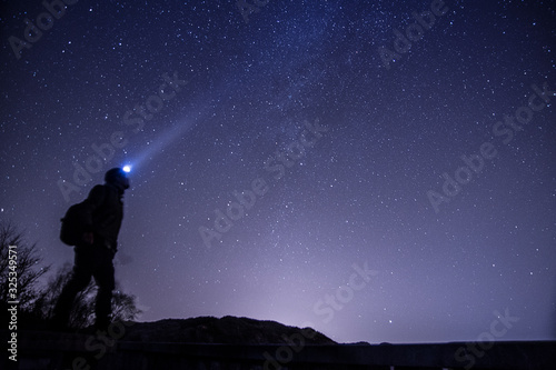 Man with headlight looking up to the sky under the night stars 