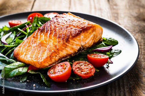 Fried salmon steak with vegetables on wooden table