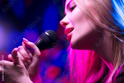 Beautiful Singing Girl, Beauty Glamour fashion Woman with Microphone over Blinking bokeh night background. Glamour Model Singer. Karaoke song, party. Rock star singer on music concert.