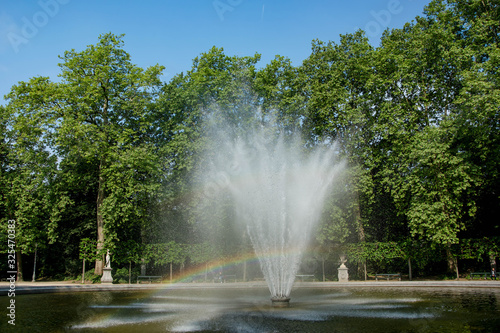 Fountain with a rainbow in beautiful garden. Green city park at sunny summer day.