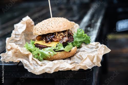 Duży burger w amerykańskim stylu na drewnianym blacie. Kanapka z grillowanym mięsem ze świeżymi warzywami i serem. Hamburger owinęty w papier ekologiczny podany na wynos
