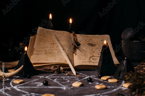 Open old book with magic spells, runes, black candles on witch table. Occult, esoteric, divination and wicca concept.