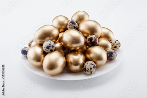 Golden eggs mixed with quail in a plate, on a white background. The concept of Easter, a symbol of the holiday, abundance and wealth.