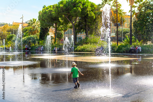 A young boy with a hat plays and splashes in the Promenade du Paillon Park in the touristic old town area of Nice, France on the French Riviera.