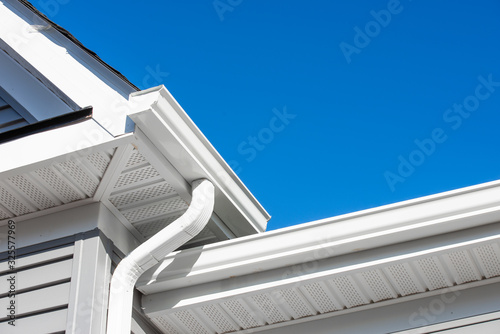 Colonial white gutter guard system, soffit providing ventilation to the attic, with gray vinyl horizontal siding at a luxury American single family home neighborhood USA