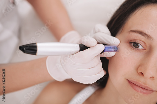 Cropped shot of a professional cosmetologist using dermapen on her female client. Young woman receiving mesotherapy treatment