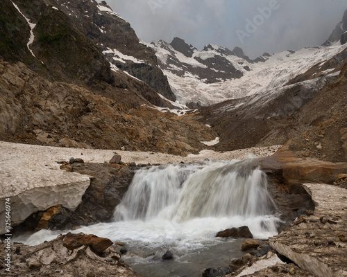mountain river from a glacier among the rocks against the background of peaks with snow Alibek, Dombay