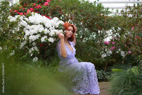 beautiful red-haired girl in arranger where azalea blooms in a colorful flying dress