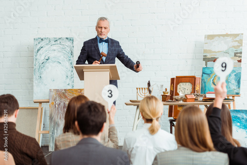 selective focus of auctioneer holding gavel and microphone and looking at buyers during auction