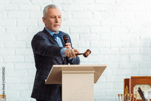 handsome auctioneer in suit holding microphone and pointing with gavel during auction