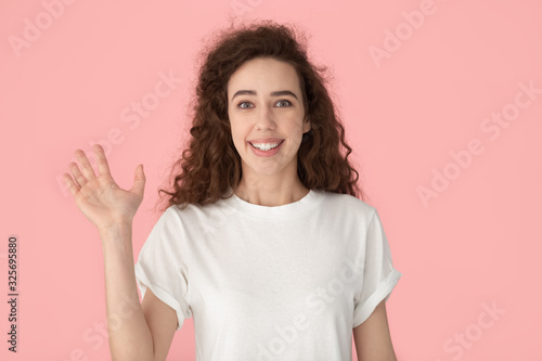 Young smiling lady waving hand, making hello gesture.