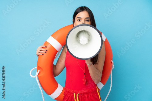 Lifeguard woman over isolated blue background with lifeguard equipment and shouting through a megaphone