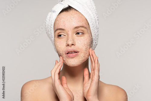 attractive girl with towel on head applying coconut scrub on face, isolated on grey