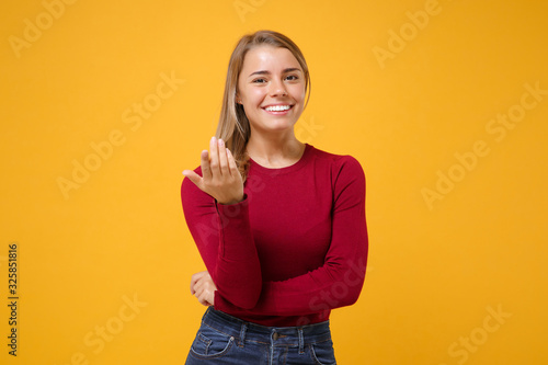 Smiling young blonde woman girl in casual clothes posing isolated on yellow orange background in studio. People lifestyle concept. Mock up copy space. Doing calling gesture like says come here to me.