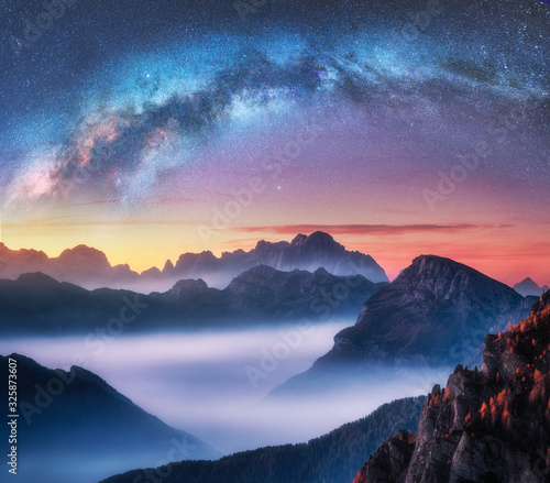 Milky Way above mountains in fog at night in summer. Landscape with alpine mountain valley, low clouds, colorful starry sky with milky way at sunset. Aerial view. Passo Giau, Dolomites, Italy. Space