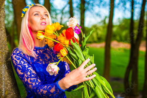 Portrait of Cute and Sensual Romantic Caucasian Blond Girl with Bunch of Tulips Posing Outdoors.