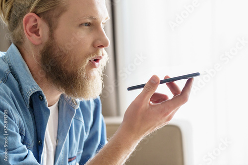 Young man hold phone speak on speakerphone using virtual digital voice recognition assistant search on smartphone at home record audio message, mobile app ai tech concept, close up side view.