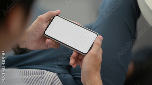 Close up view of male entrepreneur holding horizontal smartphone while lying relaxed