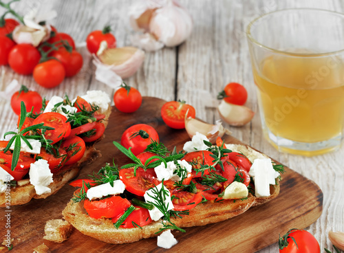 Bruschetta, toast with tomatoes, feta cheese and fresh aromatic herbs on a old rustic table. Nearby glass with homemade white wine. Traditional italian appetizer or snack, antipasto. Close up