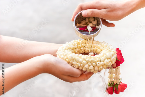 Family are watering on the elderly or respected grandparents Hand of young pour water and flowers on the Elder hands holding jasmine garland for the songkran festival.