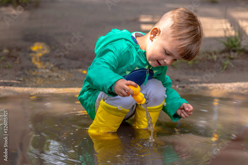 a small child plays sitting in a puddle in rainy weather
