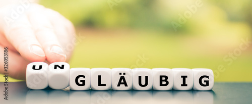 Hand dreht Würfel und ändert das Wort "gläubig" in "ungläubig"