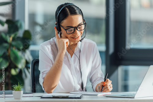 smiling asian translator working online with headset and laptop in office